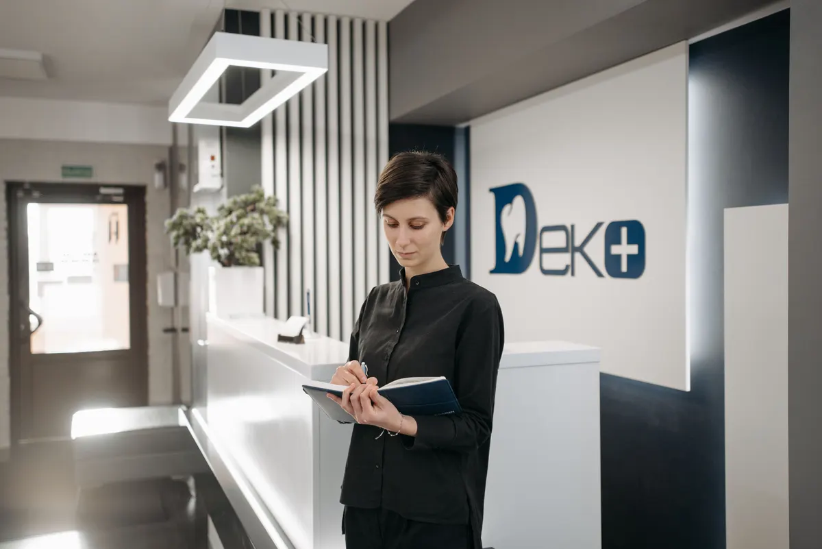 Recepcionista de una clínica dental anotando a mano en un cuaderno, en el mesón de atención.